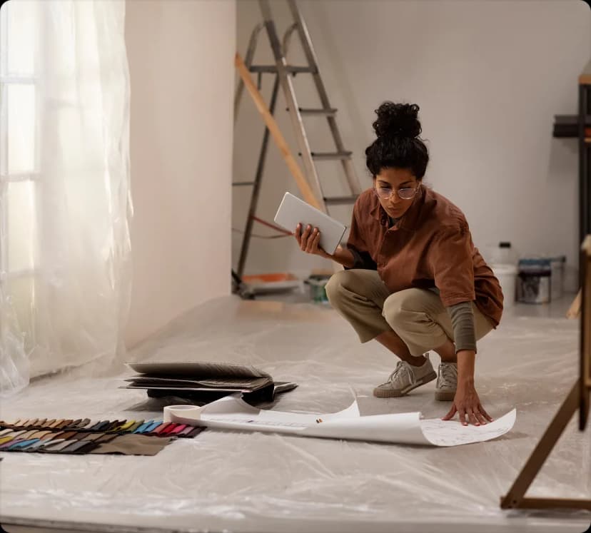 A woman kneeling on a dust sheet while renovating a stripped-back room